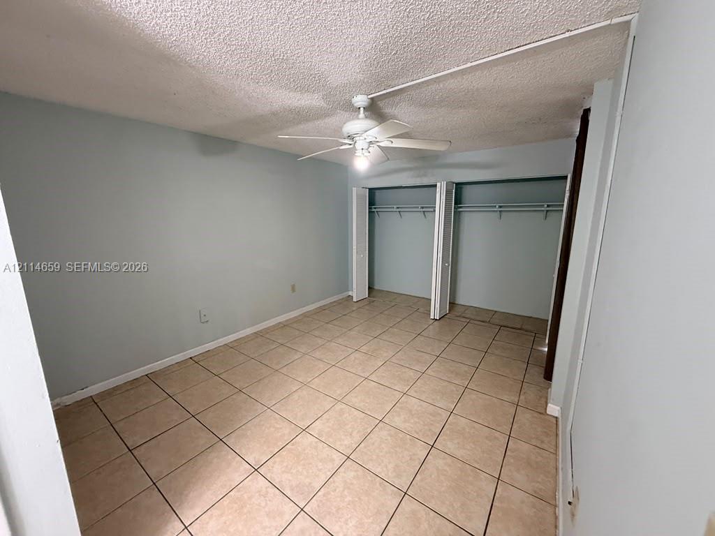 Room featuring neutral-toned tile flooring, ceiling-mounted fan with light fixture, and walk-in closet with double bifold doors