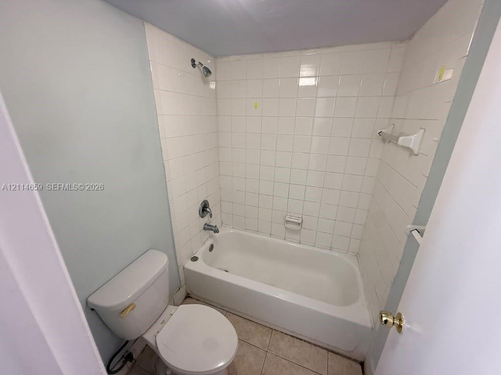 Full bathroom featuring a white porcelain soaking tub, tile surround, wall-mounted shower head, and tile flooring