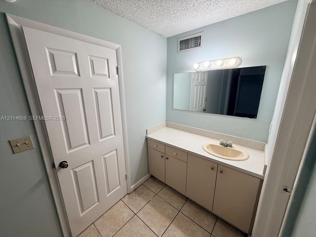 Vanity featuring a solid-surface countertop, integrated basin, cabinetry with hardware, a wall-mounted mirror, and tile flooring