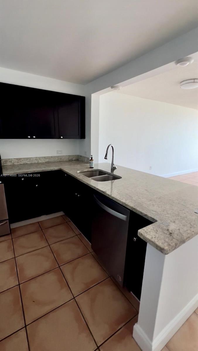 Kitchen featuring dark wood-finish cabinetry, stone countertops, stainless steel dual-basin sink, high-arch faucet, and tile flooring Kitchen featuring dark wood-finish cabinetry, stone countertops, stainless steel dual-basin sink, high-arch faucet, and tile flooring
