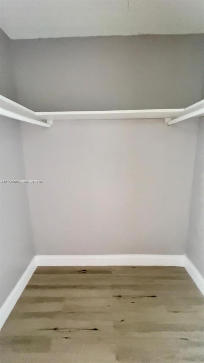 Walk-in closet featuring wood-finish flooring and built-in shelving with integrated rods Walk-in closet featuring wood-finish flooring and built-in shelving with integrated rods