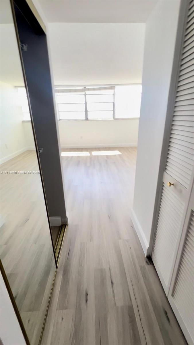 Interior space featuring light-toned wood-finish flooring, floor-to-ceiling mirrored closet doors, and louvered closet cabinetry with metallic hardware