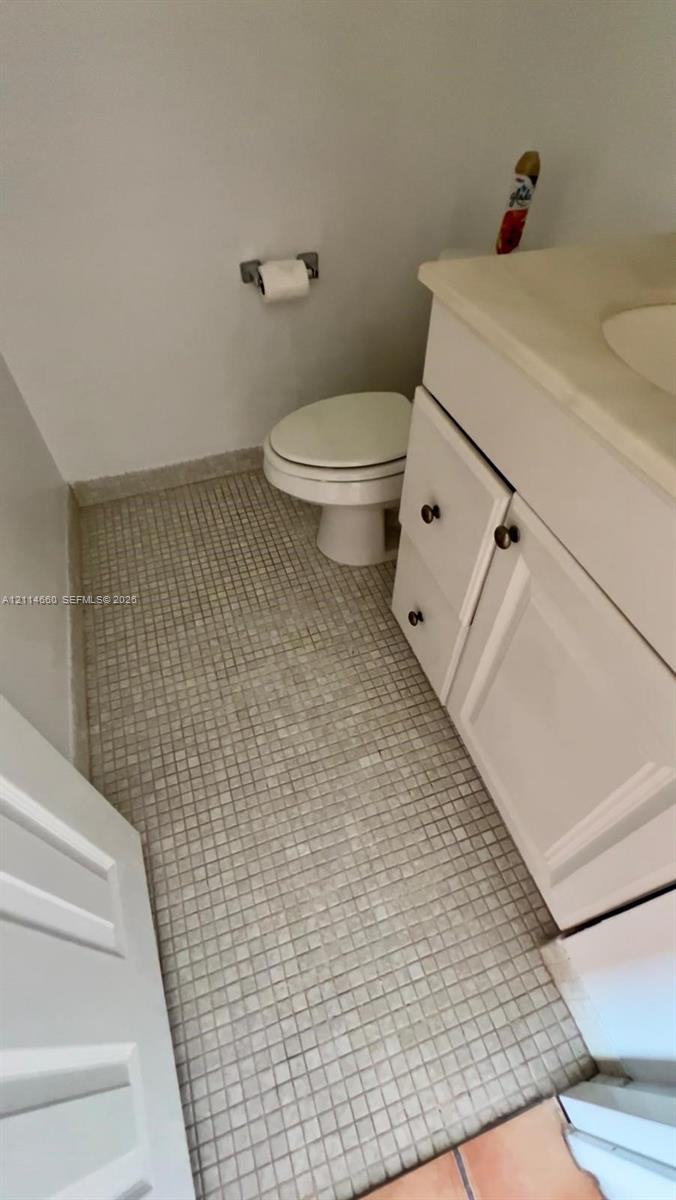 Bathroom featuring a vanity with an integrated basin, white cabinetry, mosaic tile flooring, and a wall-mounted paper holder Bathroom featuring a vanity with an integrated basin, white cabinetry, mosaic tile flooring, and a wall-mounted paper holder