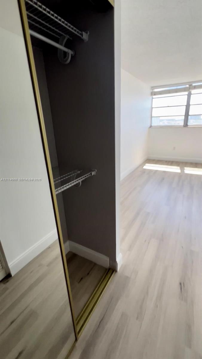 Closet with sliding mirrored doors, interior wire shelving, wood-finish flooring, and horizontal window blinds