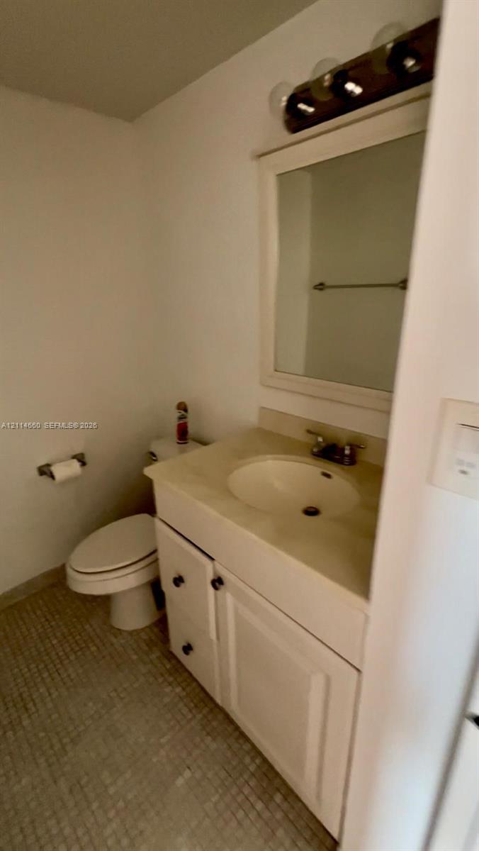 White vanity cabinet with an integrated sink, neutral countertop, rectangular framed mirror, and multi-bulb vanity lighting White vanity cabinet with an integrated sink, neutral countertop, rectangular framed mirror, and multi-bulb vanity lighting