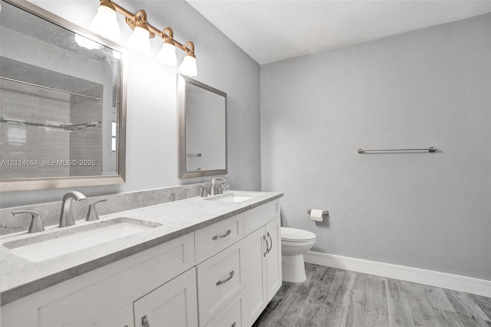 Double vanity featuring white cabinetry, stone-finish countertops, dual rectangular undermount sinks, and a multi-light polished metal fixture