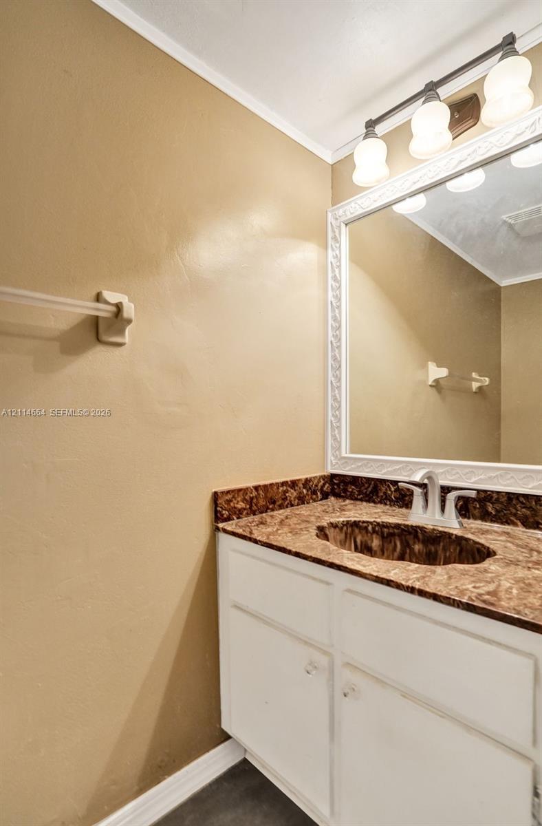 Vanity featuring a white cabinet, integrated sink, stone-finish countertop, decorative framed mirror, and three-bulb vanity light fixture