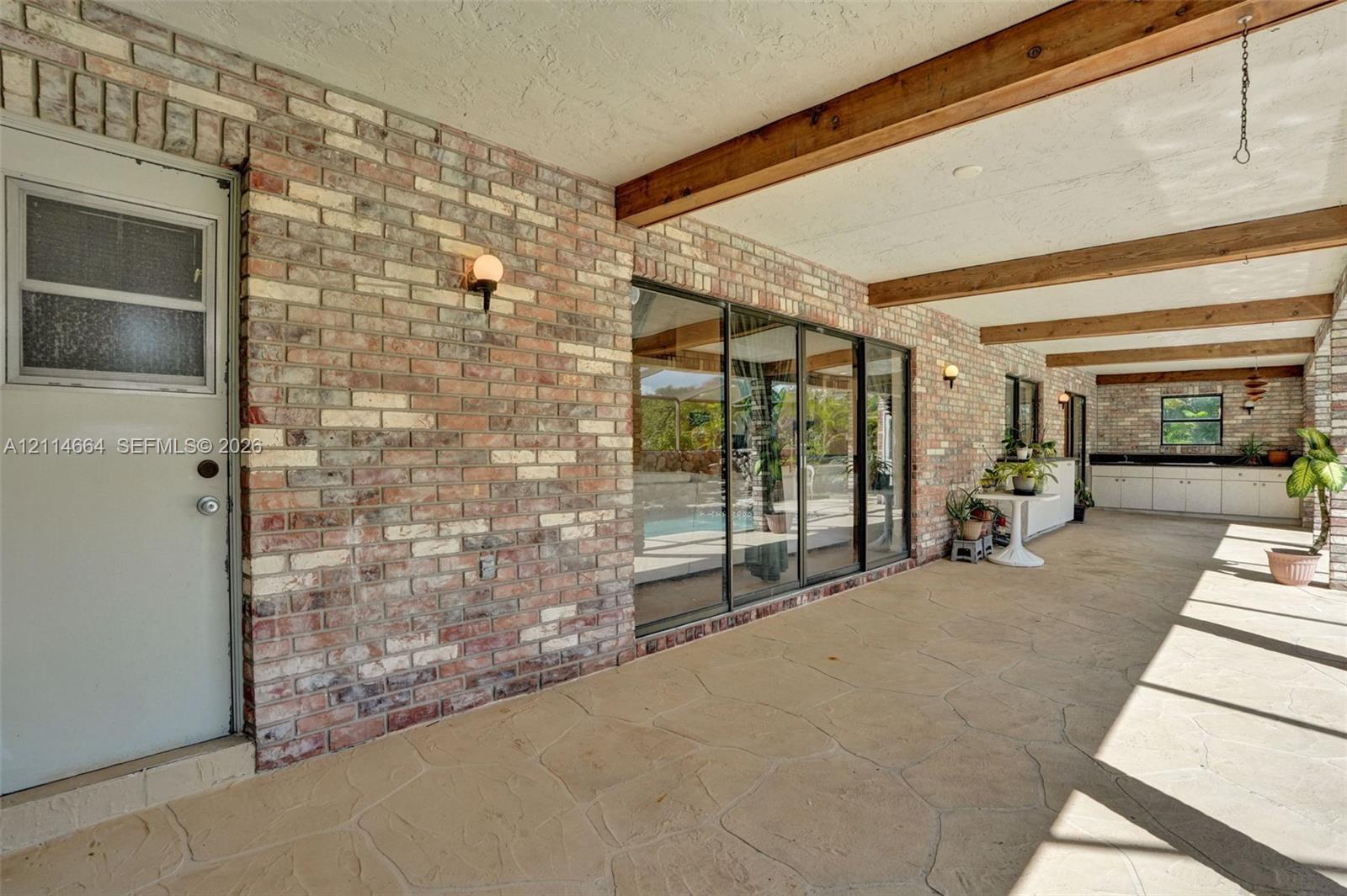 Covered patio featuring exposed wood ceiling beams, multi-tonal brick masonry, flagstone-style flooring, sliding glass doors, and built-in cabinetry