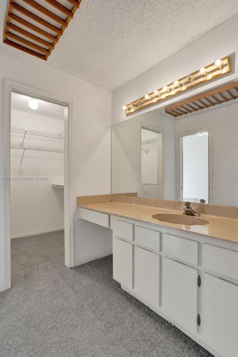 Vanity featuring white cabinetry, a solid surface countertop, an integrated sink, and an expansive wall-mounted mirror