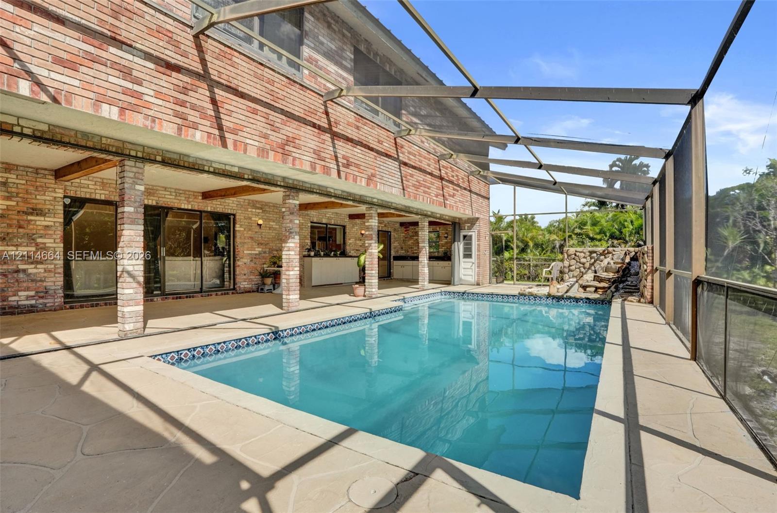 Screened lanai featuring a swimming pool, stone-accented water feature, brick exterior wall, and covered patio space