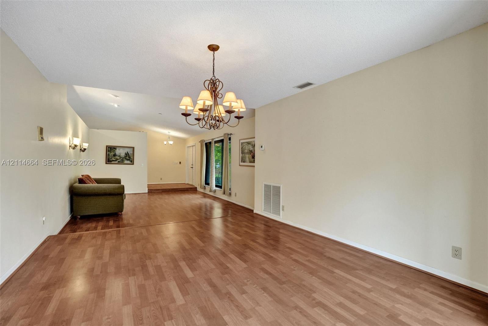 Open interior featuring wood-finish flooring, a multi-arm metal chandelier, wall-mounted light fixtures, and windows with neutral framing
