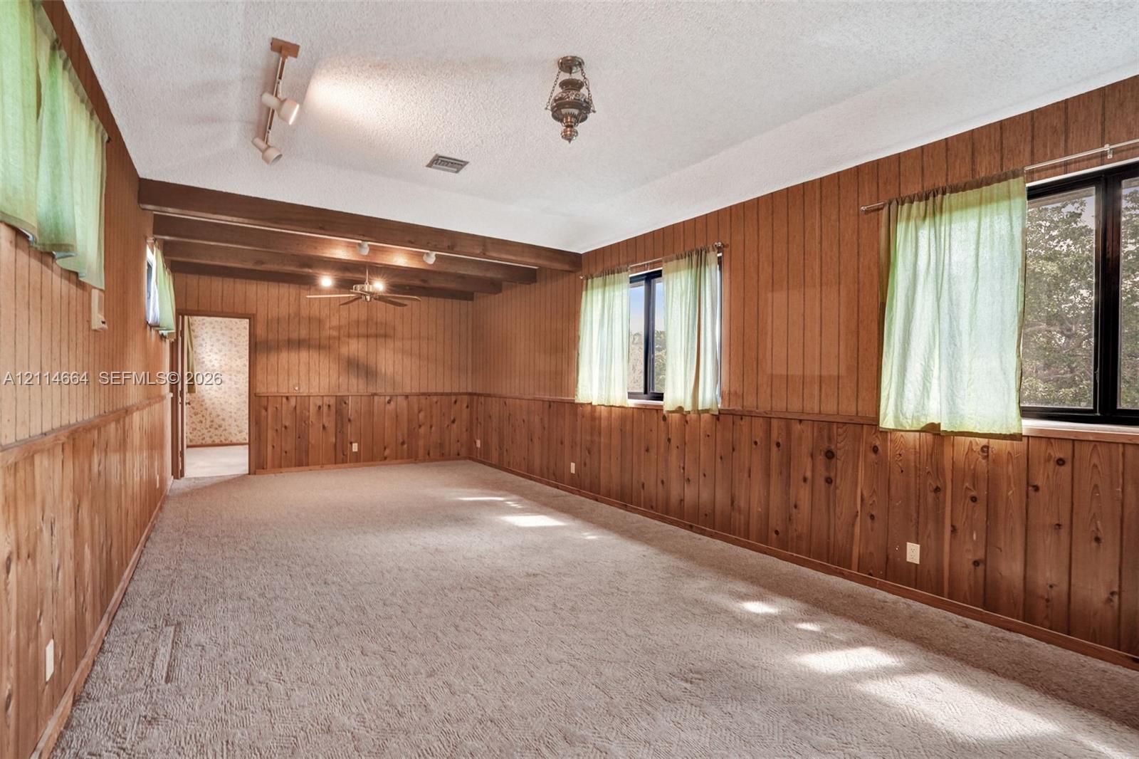 Interior space featuring wood paneling, vaulted ceiling with exposed beams, recessed track lighting, and carpeted flooring