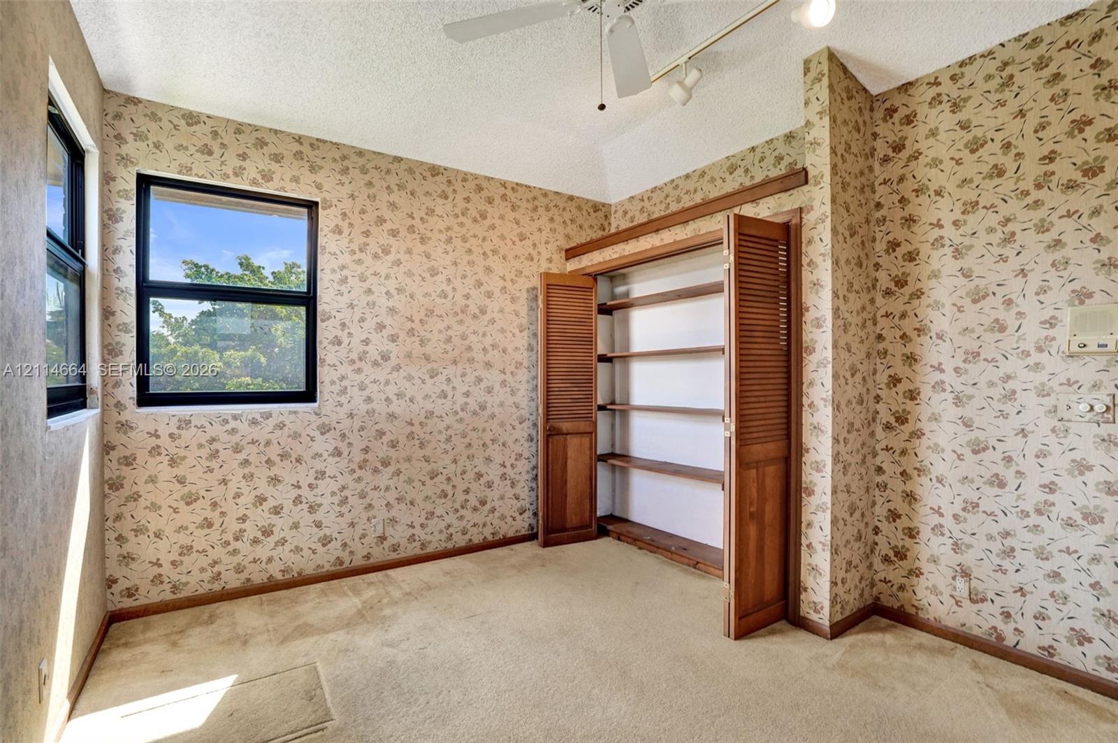 Interior space featuring built-in wooden shelving with louvered doors, carpeting, a ceiling-mounted fan, and dual-pane windows
