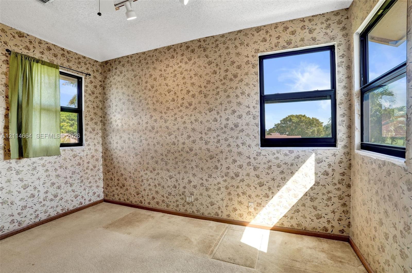Interior space featuring patterned wallpaper, carpeting, and three windows with dark frames