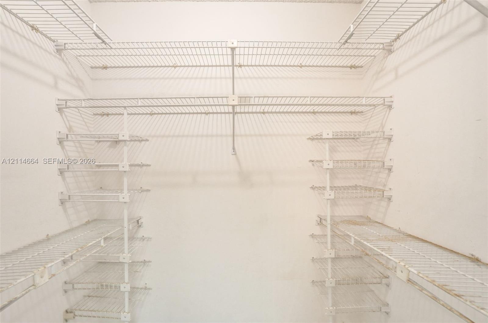 Walk-in storage area featuring white wire shelving units with multi-level hanging rods and integrated shelf tiers