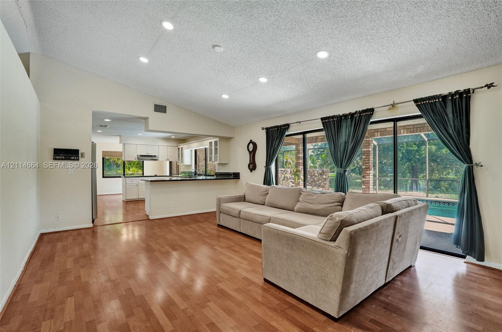Open-concept floor plan featuring vaulted ceilings, recessed lighting, wood-finish flooring, and large sliding glass doors