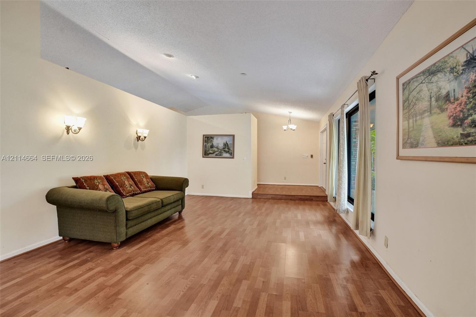 Living space featuring vaulted ceilings, wood-finish flooring, wall-mounted light fixtures, and a raised platform area