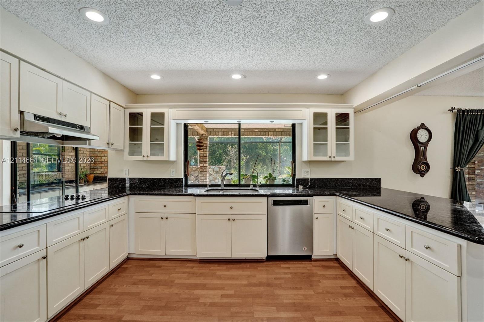 Kitchen featuring off-white cabinetry, dark stone countertops, stainless steel appliances, recessed ceiling lighting, and wood-finish flooring