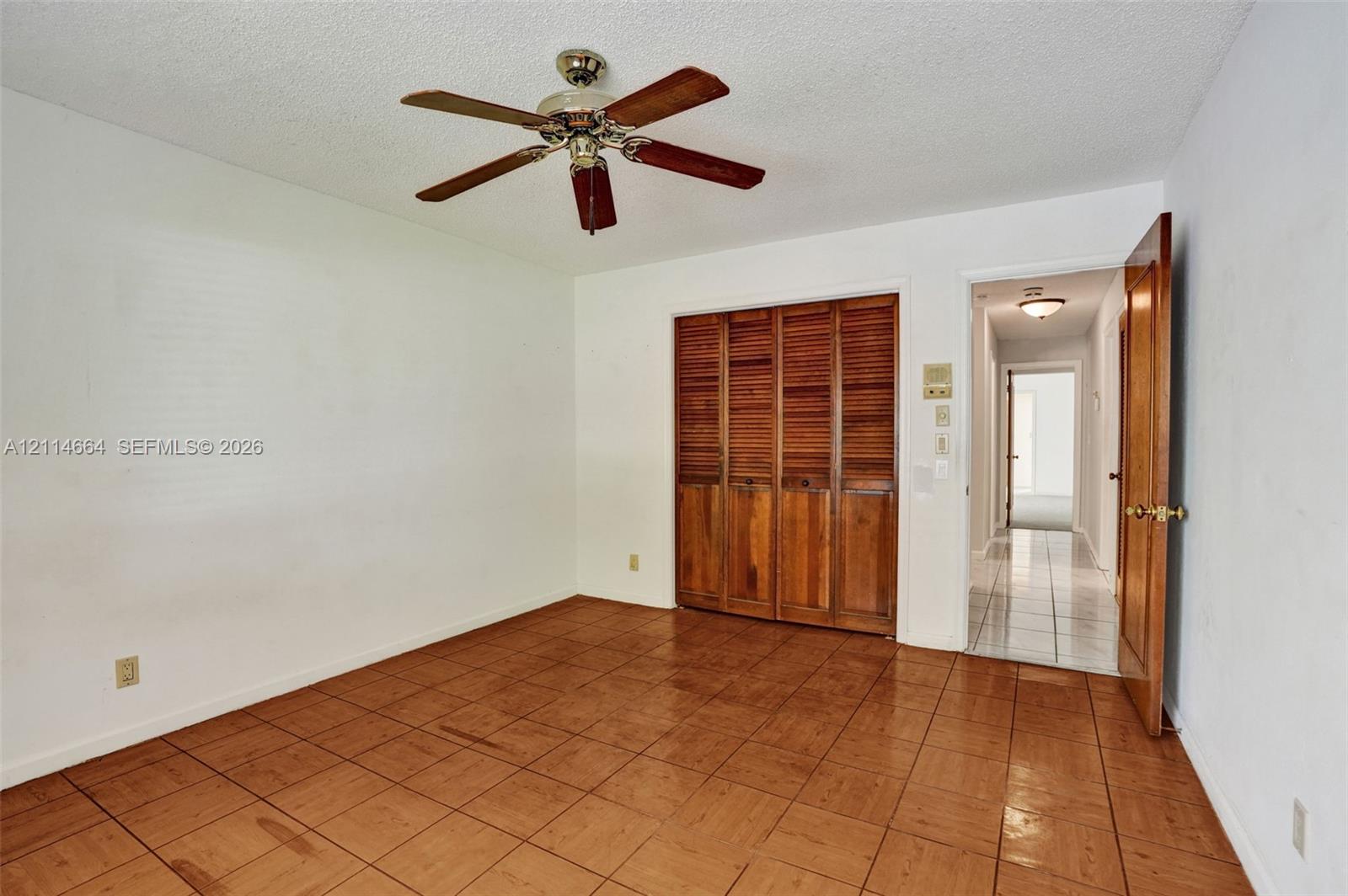 Room featuring square ceramic tile flooring, built-in wooden louvered closet doors, and a ceiling fan with integrated lighting
