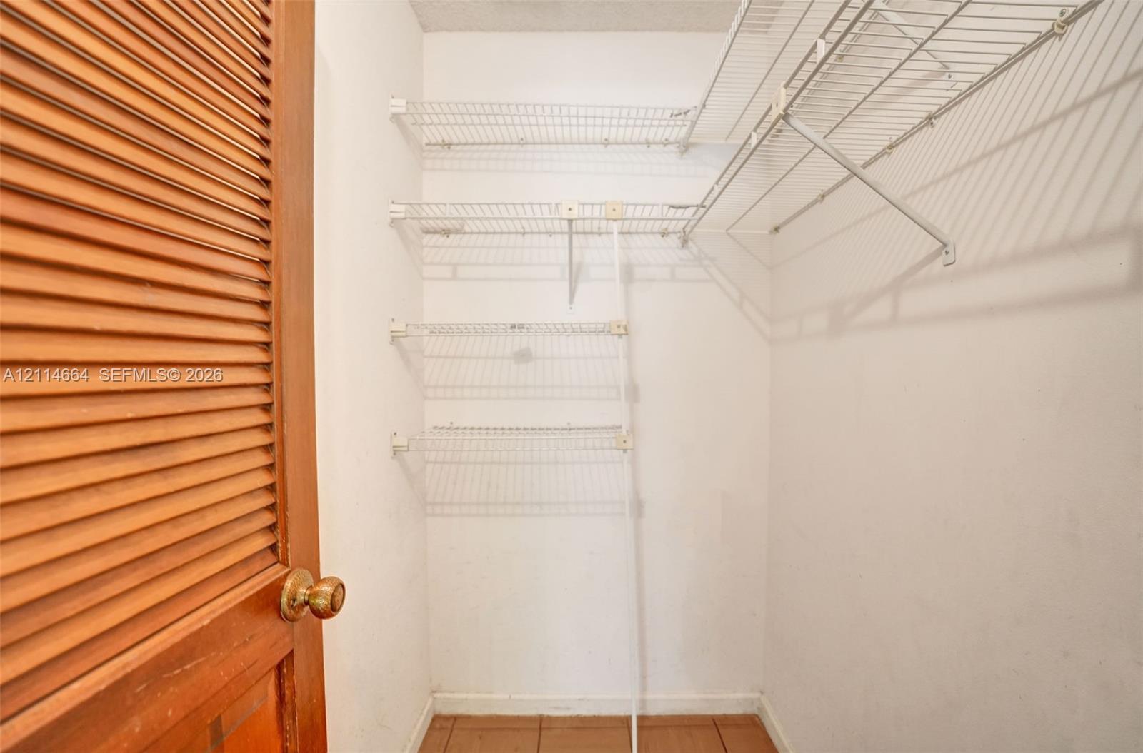 Storage space featuring wood-finish louvered bi-fold doors, white interior walls, wire shelving, and tiled flooring