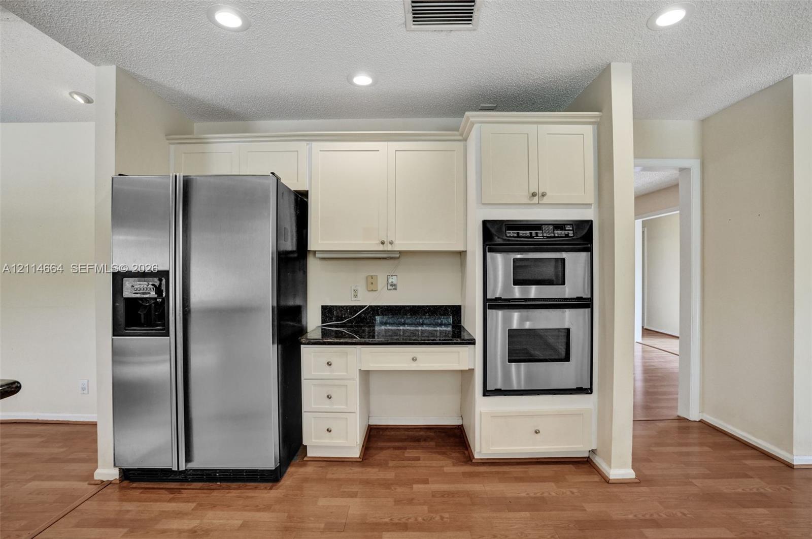 Kitchen featuring off-white cabinetry, dark stone countertops, stainless steel double wall ovens, side-by-side refrigerator, and wood-finish flooring