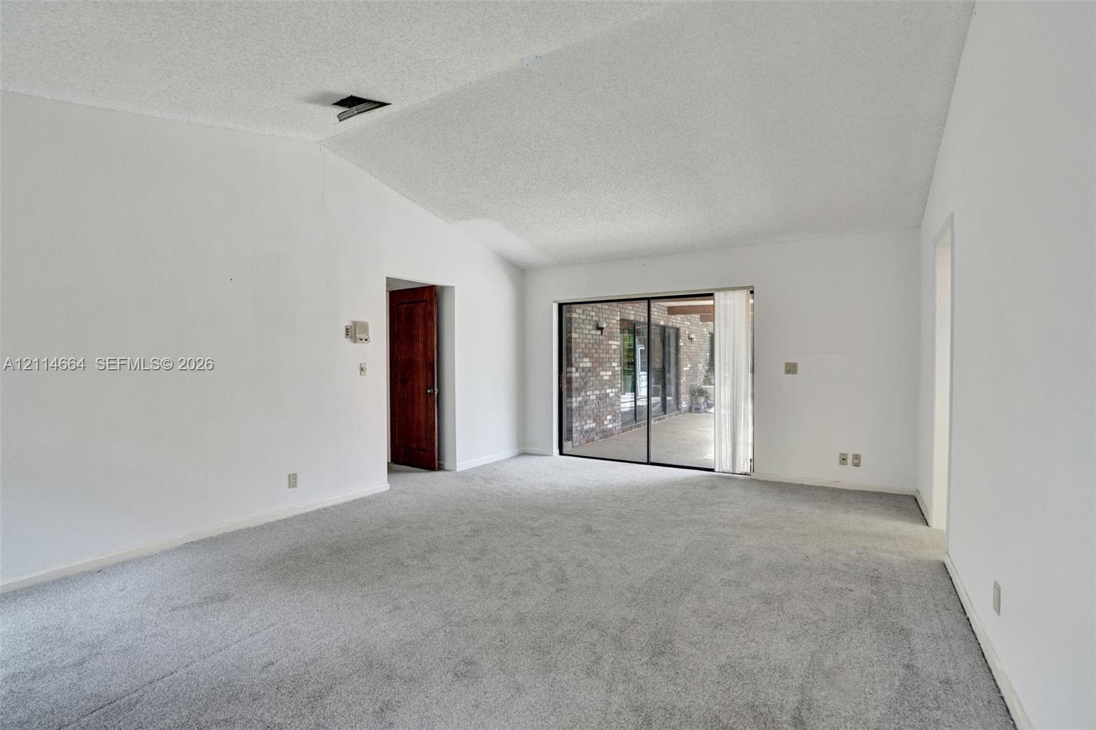 Vaulted ceiling, wall-to-wall carpeting, and floor-to-ceiling sliding glass doors opening to a brick-accented patio