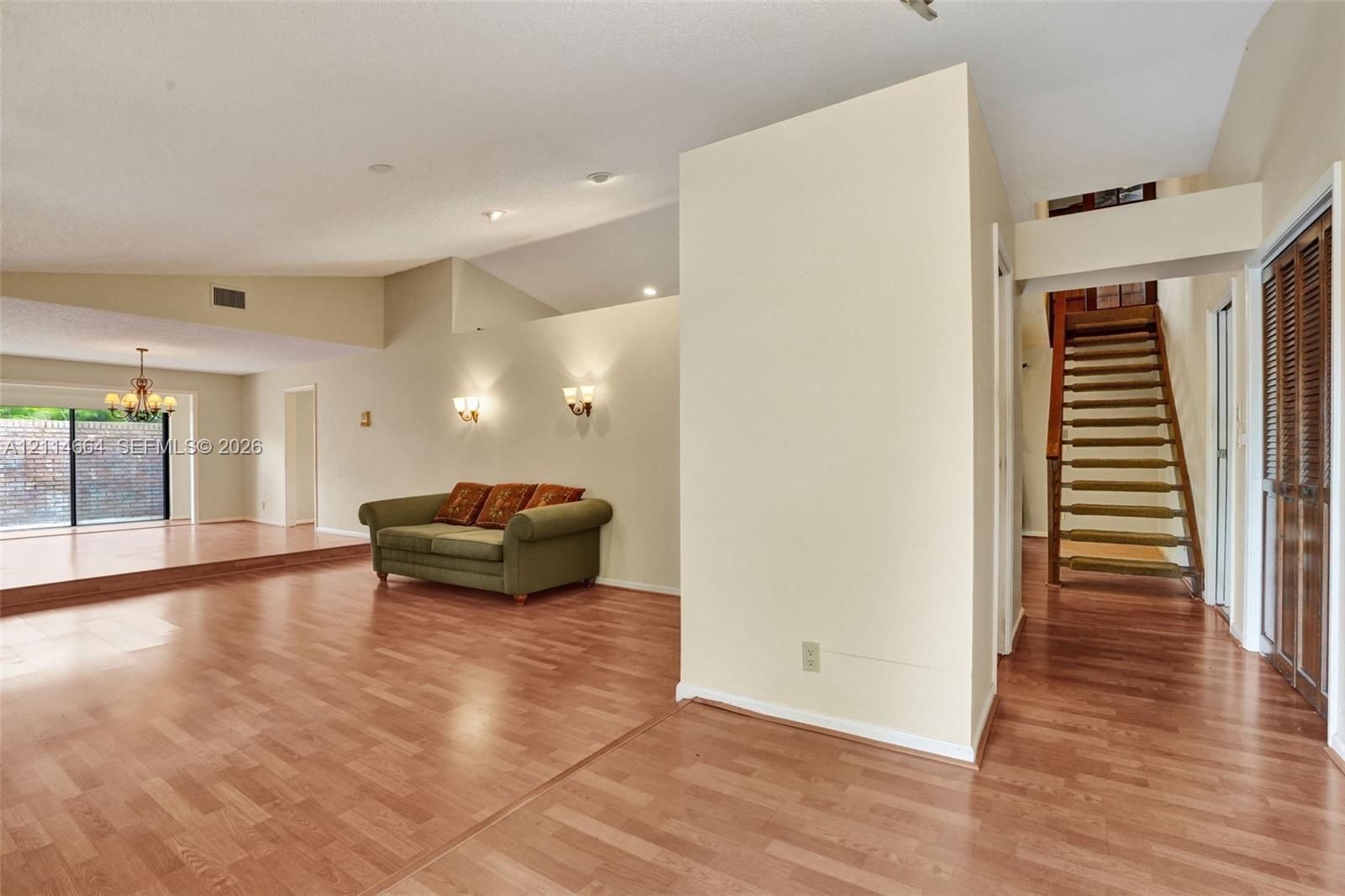 Vaulted ceilings with recessed lighting, wood-finish flooring, wall-mounted light fixtures, sliding glass doors, and a wood staircase