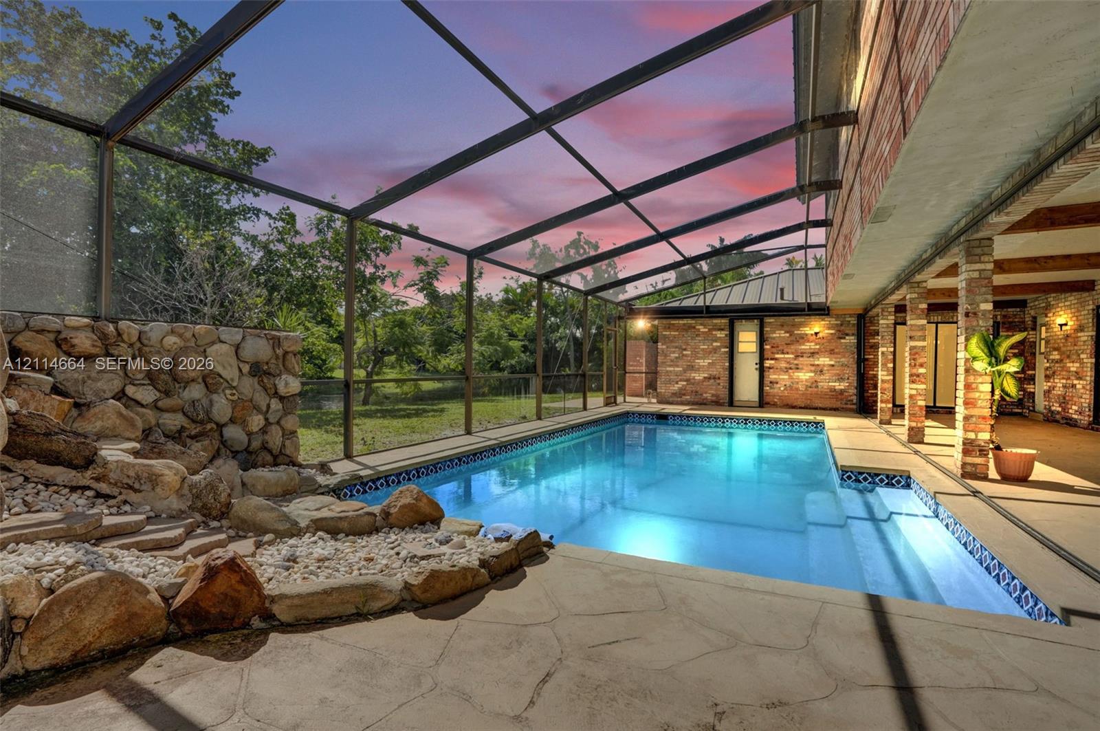 Screened-in pool area featuring a natural stone water feature, patterned stone decking, and brick exterior walls