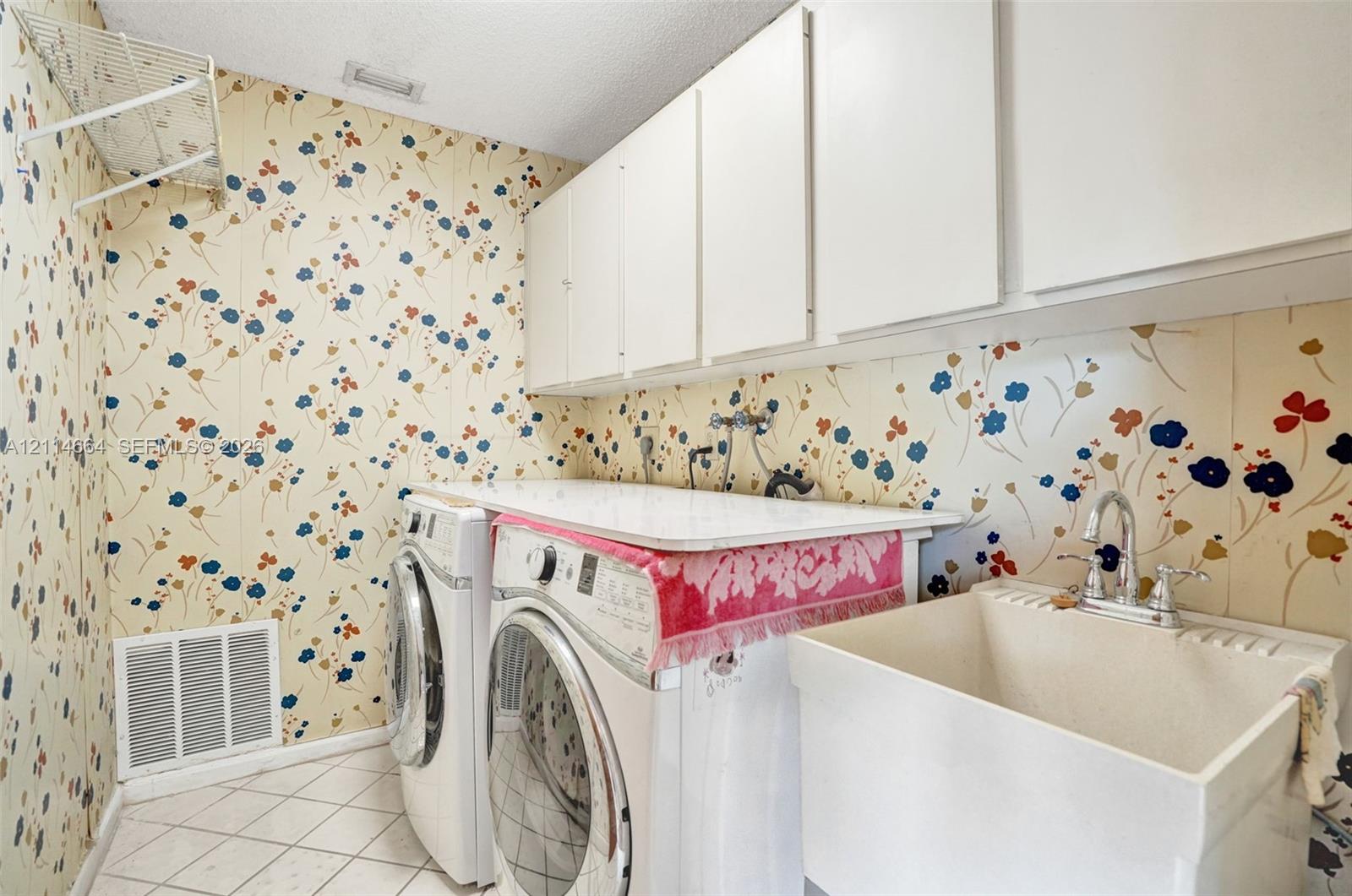 Laundry area featuring white wall-mounted upper cabinetry, a utility basin with a chrome faucet, and a flat-surface folding counter