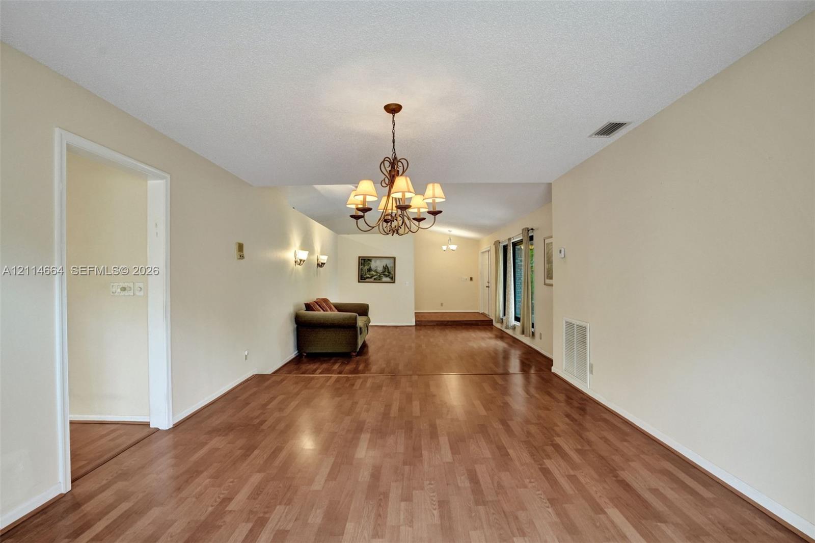Open-concept interior featuring wood-finish flooring, vaulted ceilings, a multi-arm chandelier, and wall-mounted sconces