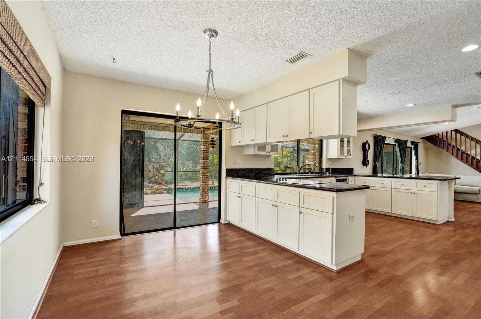 Kitchen featuring white shaker-style cabinetry, dark stone-surface countertops, wood-finish flooring, a metal multi-arm chandelier, and a sliding glass door