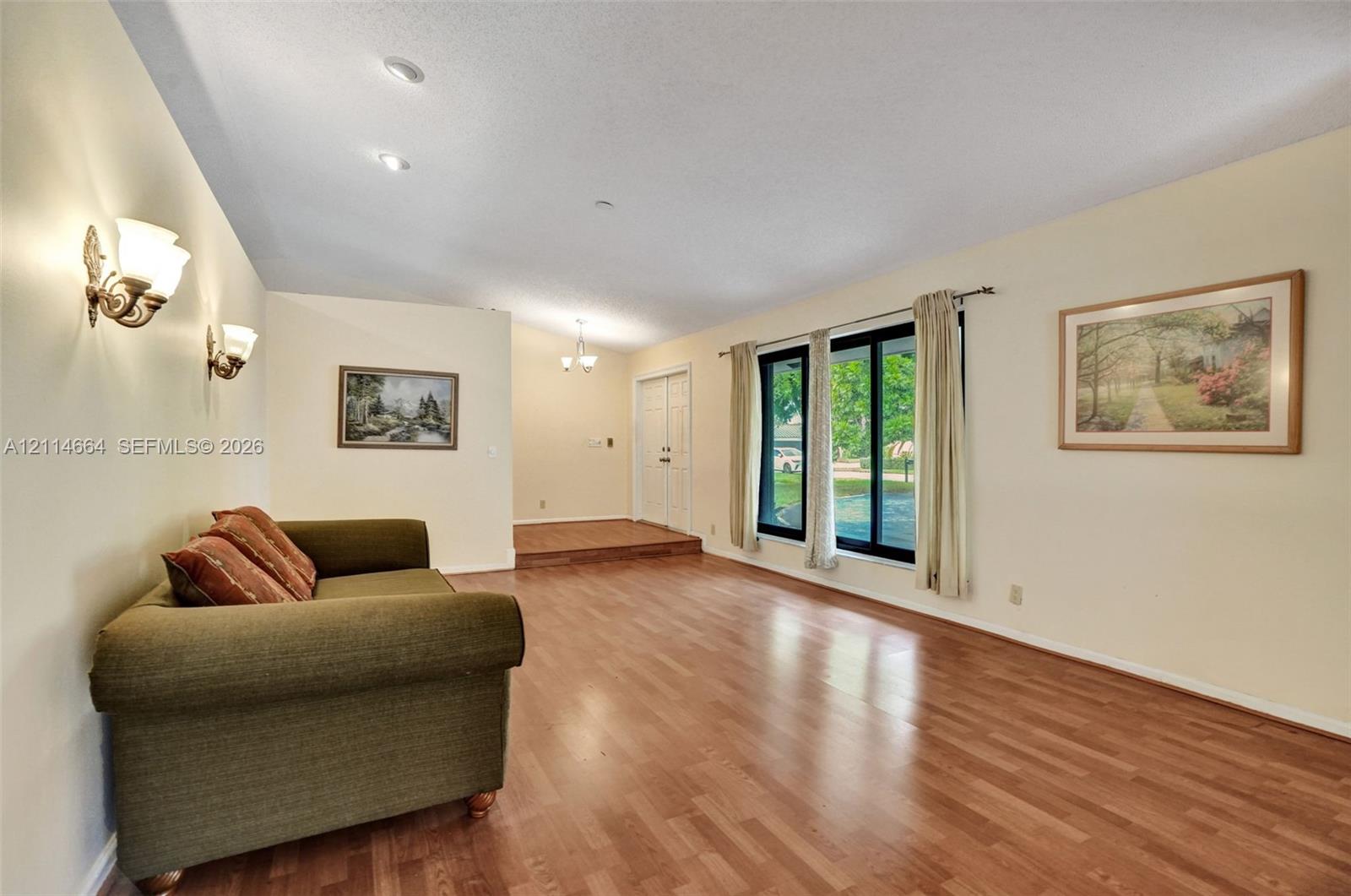 Living area featuring wood-finish flooring, recessed ceiling lighting, wall-mounted light fixtures, large windows with black frames, and a raised entryway platform with double doors