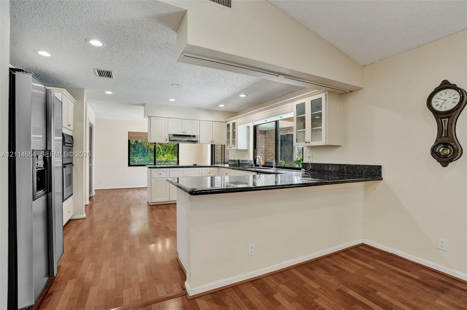 Kitchen featuring a breakfast bar, stone-surface countertops, white cabinetry with glass-panel upper doors, stainless steel wall-mounted oven, and wood-finish flooring