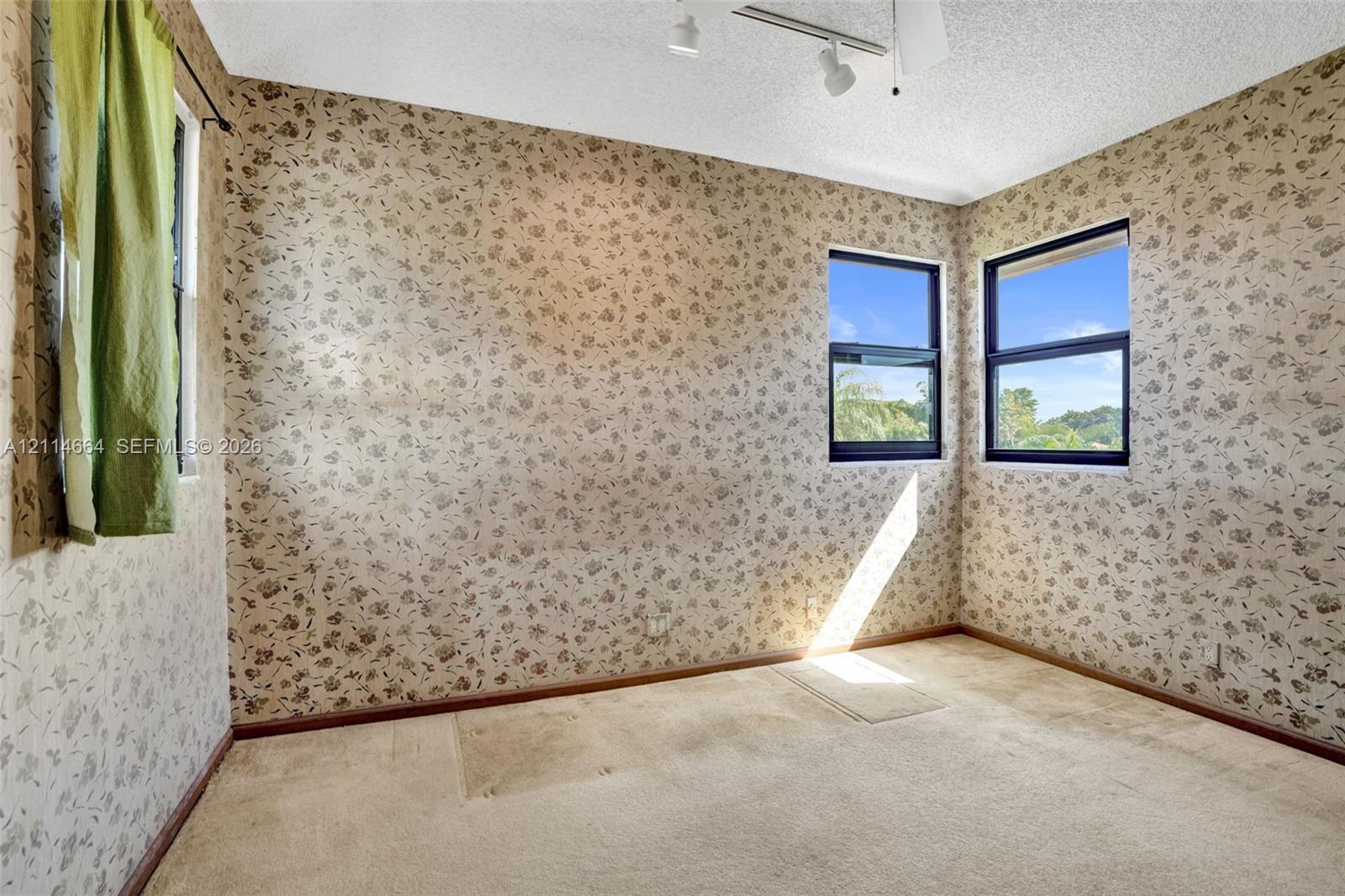 Corner room featuring patterned wallpaper, carpeting, three windows, and ceiling-mounted track lighting
