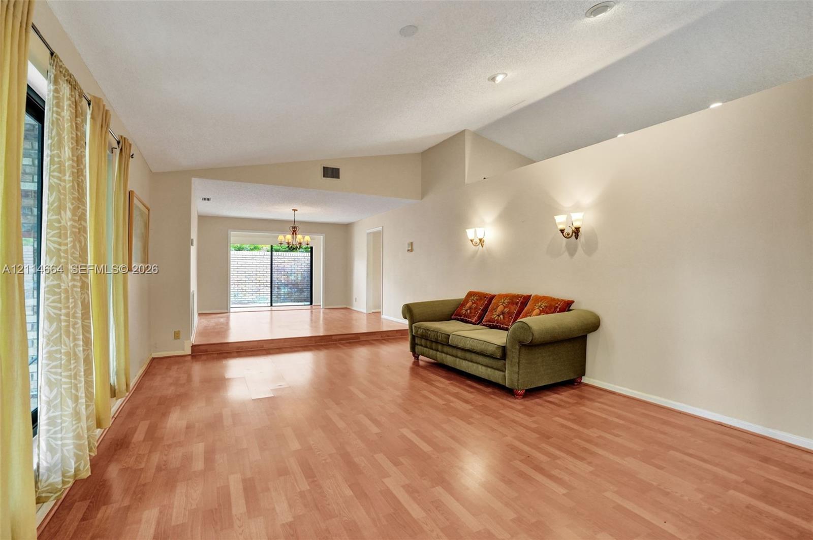 Living area featuring vaulted ceilings, wood-finish flooring, recessed lighting, wall-mounted sconces, and a raised platform level