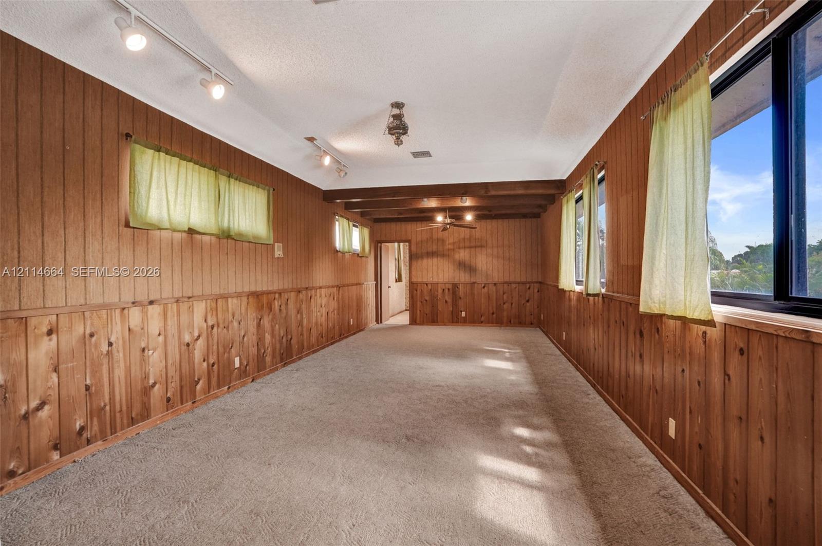 Interior space featuring wood-paneled walls, exposed ceiling beams, adjustable track lighting, and wall-to-wall carpeting
