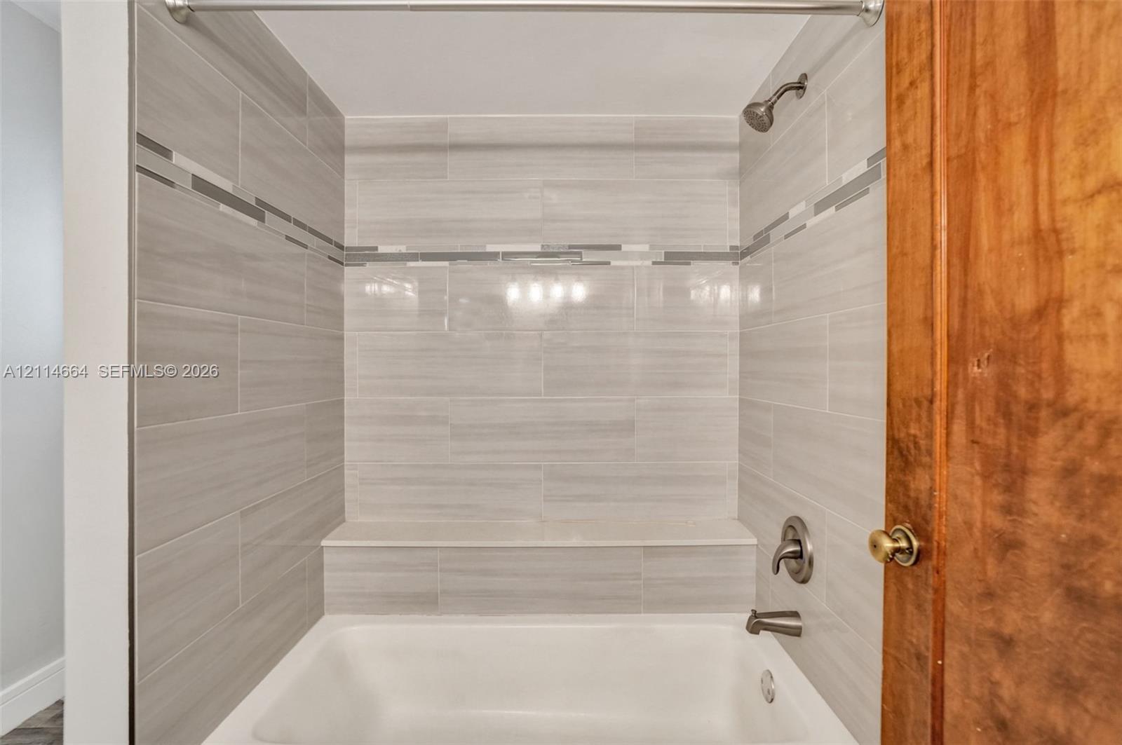 Bathtub enclosure featuring neutral-toned ceramic tile surround, decorative glass tile inlay, built-in shelving ledge, and wall-mounted metal fixtures