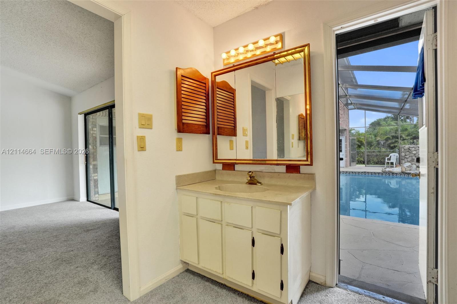 Vanity with stone-finish countertop, integrated sink, large rectangular mirror, multi-bulb overhead lighting, and dual louvered-style wall cabinets