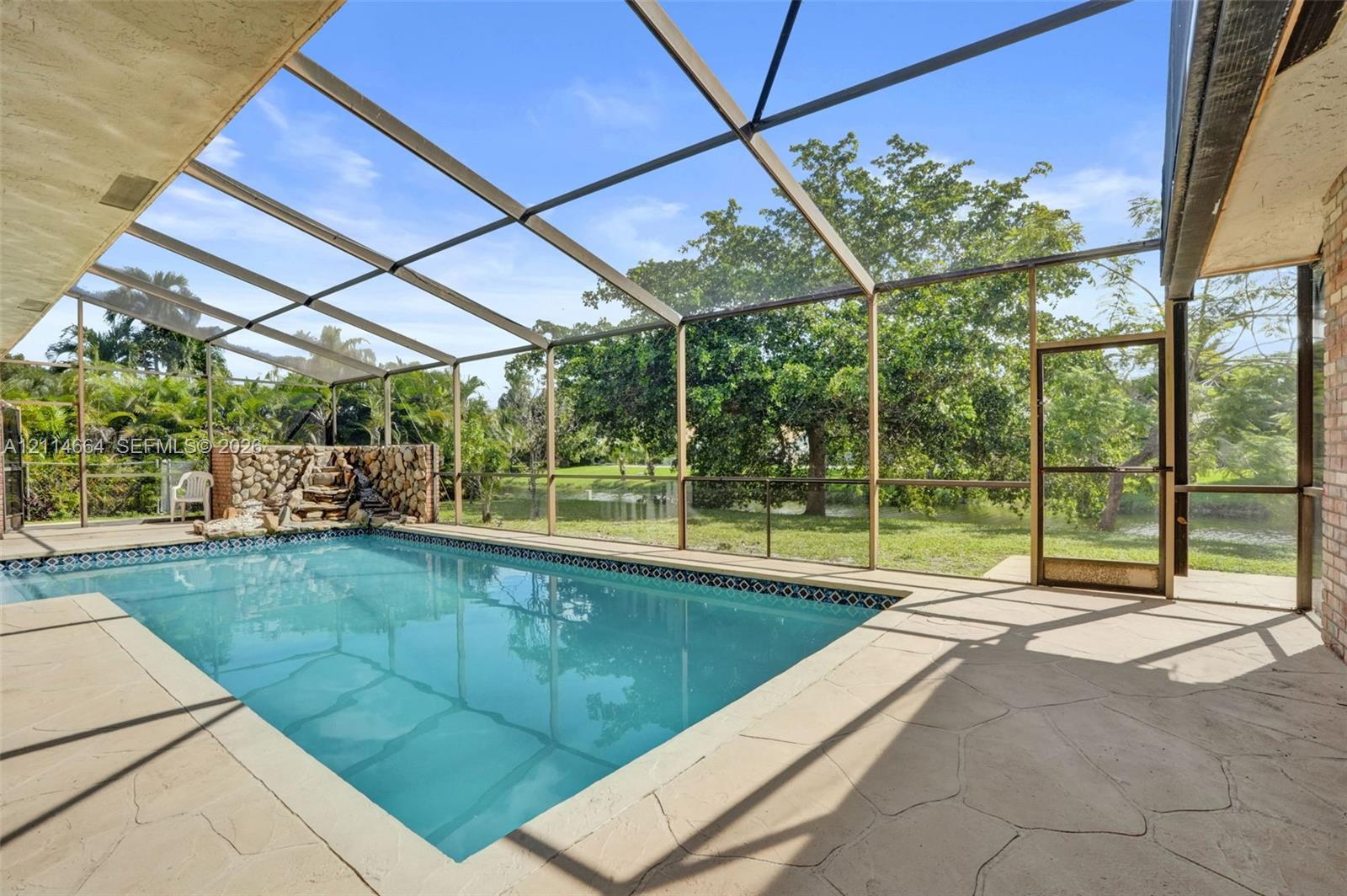 Screen-enclosed swimming pool featuring a flagstone-style patio, built-in stone waterfall feature, and direct water frontage