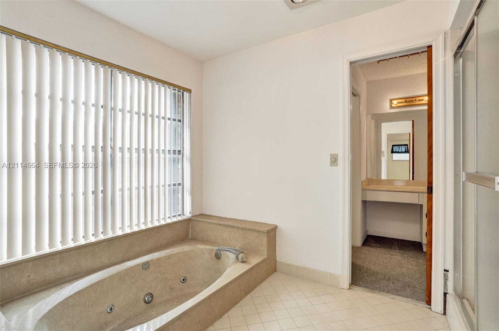 Jetted soaking tub with tile surround, window featuring vertical blinds, ceramic tile flooring, and glass-enclosed shower