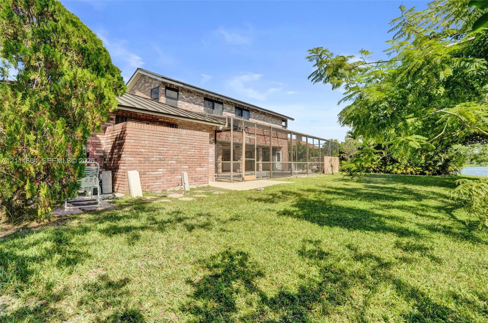 Brick exterior residence featuring a metal roof, screened-in porch, and expansive grassy yard