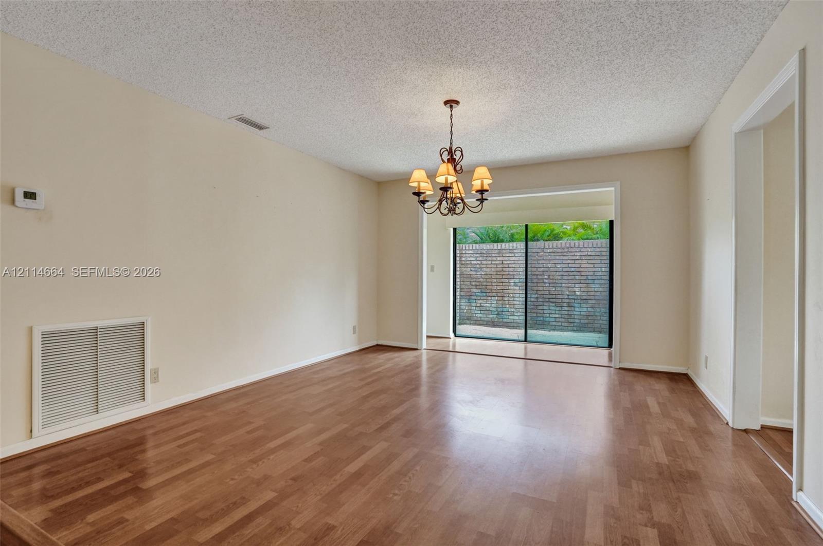 Living area featuring wood-finish flooring, a multi-arm chandelier, and sliding glass doors with exterior brick wall visibility
