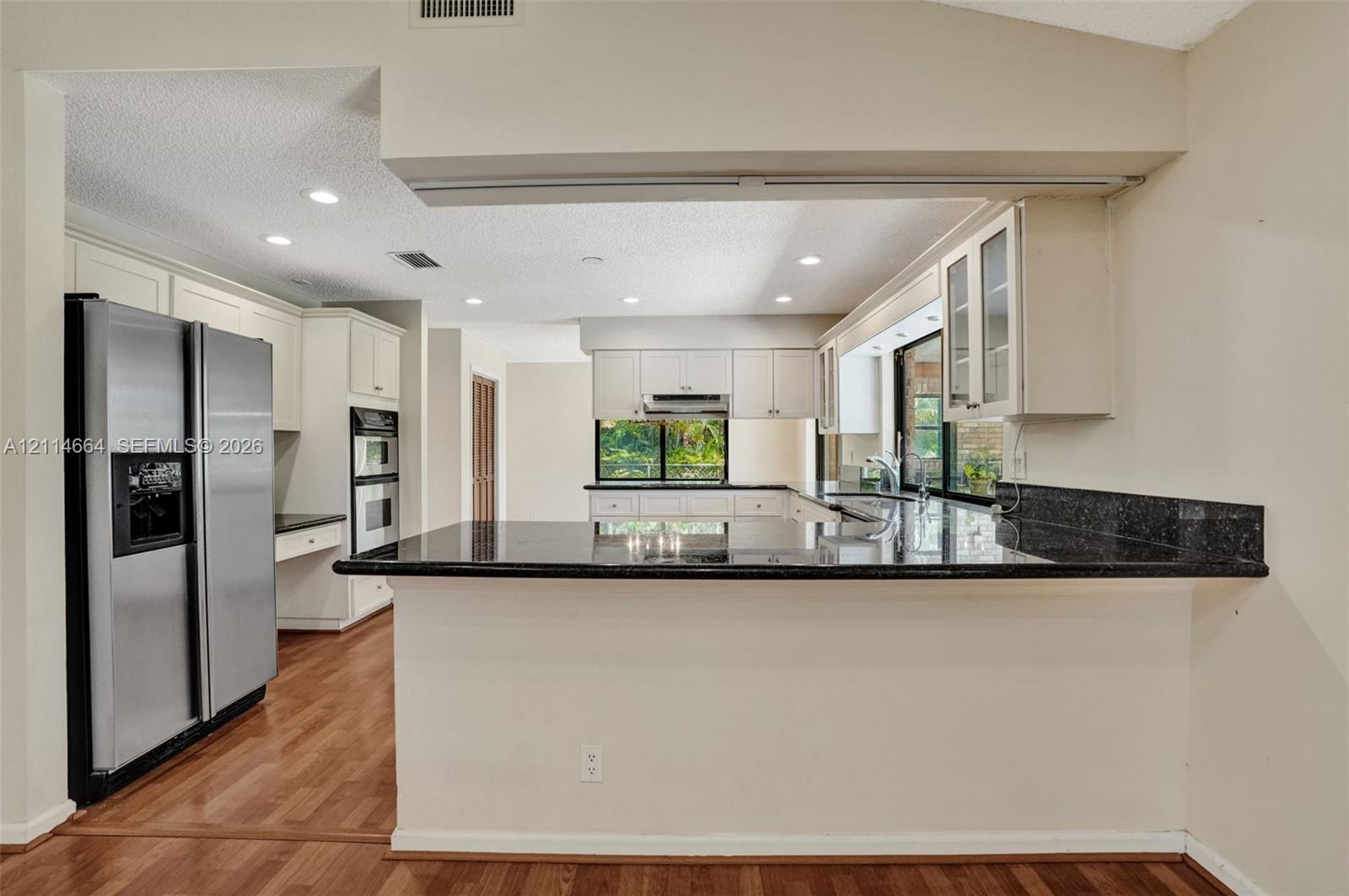 Kitchen featuring white cabinetry, dark stone-finish countertops, stainless steel side-by-side refrigerator, built-in double wall oven, and wood-finish flooring