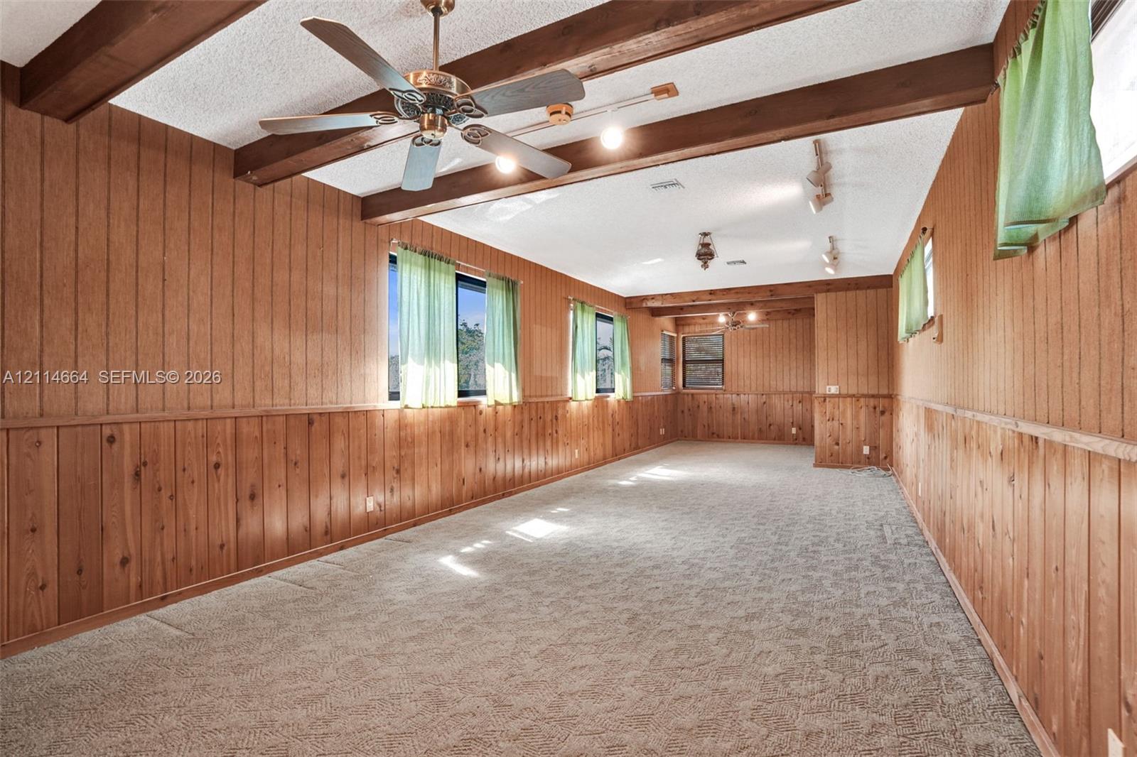 Interior space featuring wood paneling, exposed ceiling beams, carpeted flooring, a ceiling fan, and adjustable track lighting