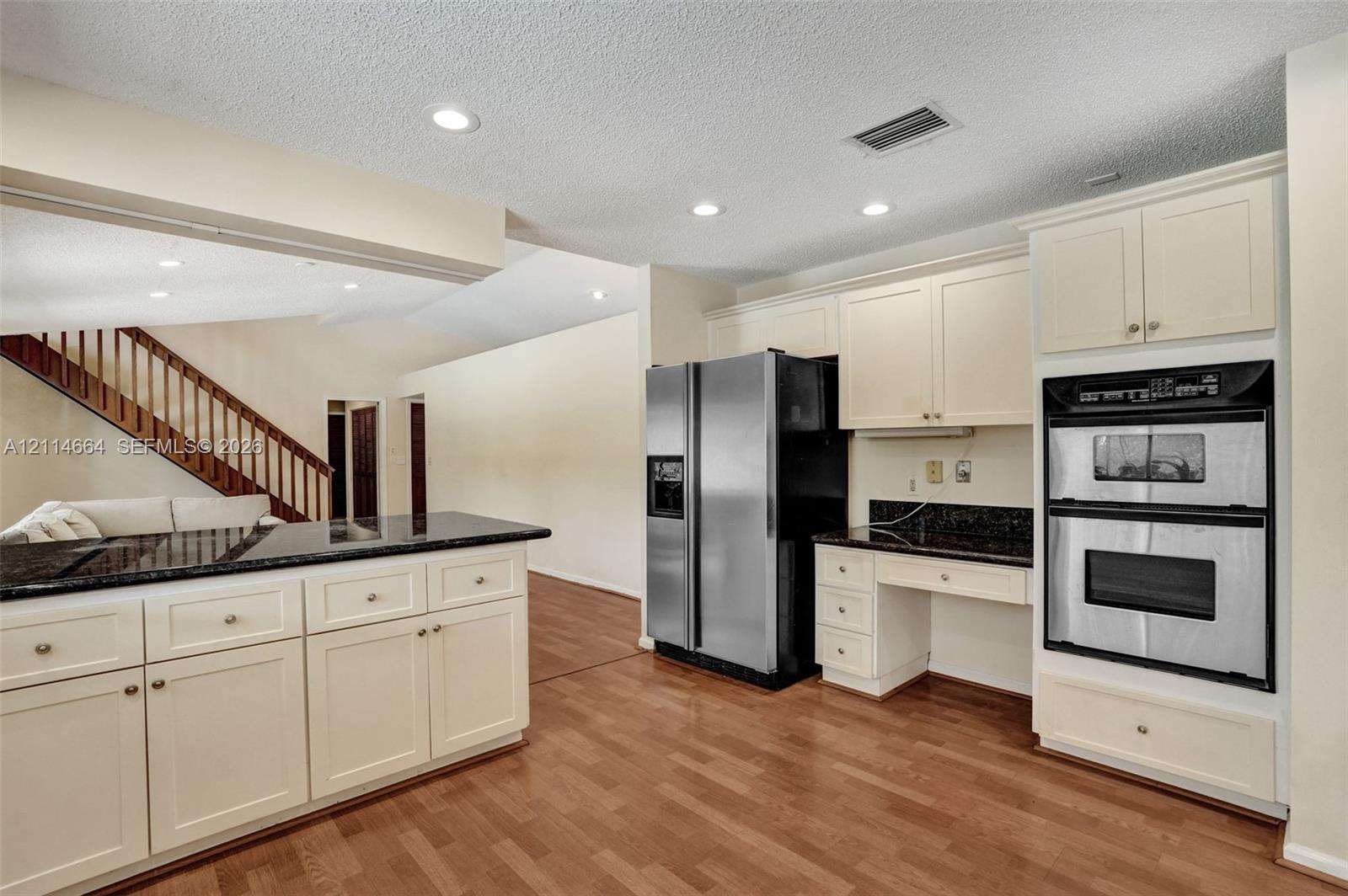 Kitchen featuring light-toned cabinetry, dark stone countertops, integrated double wall ovens, a side-by-side stainless steel refrigerator, and wood-finish flooring