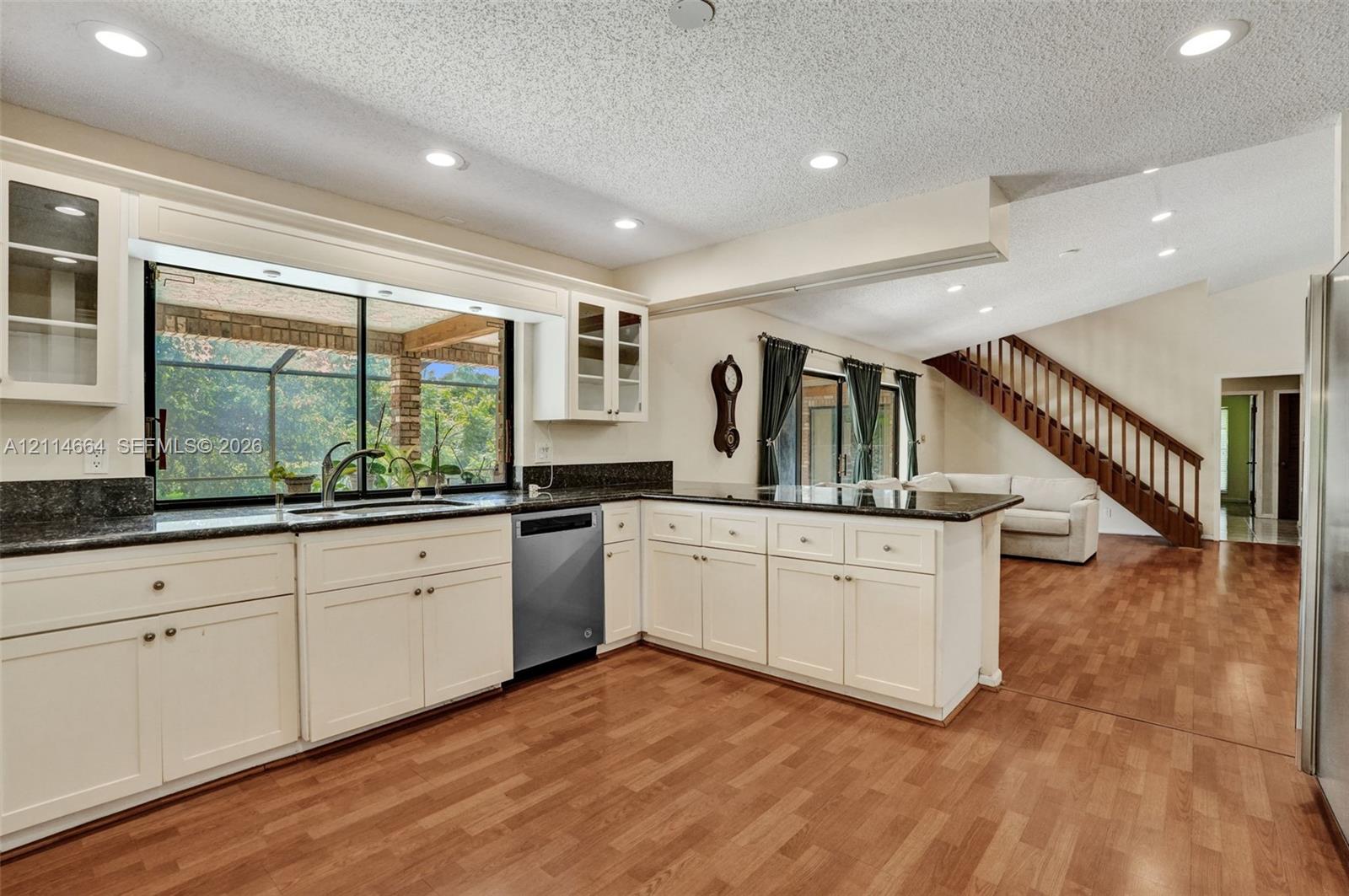 Kitchen featuring off-white cabinetry, dark stone countertops, recessed lighting, wood-finish flooring, and a stainless steel dishwasher