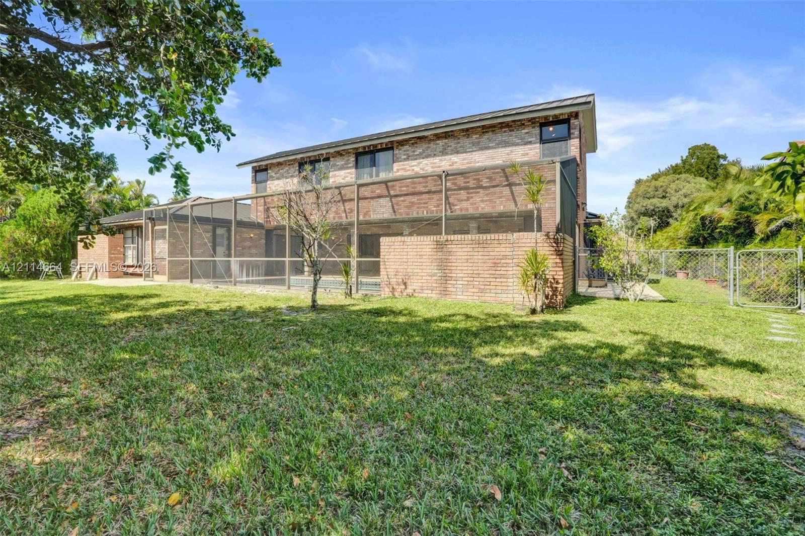Two-story brick exterior featuring an expansive backyard, a screened-in lanai, and a perimeter chain-link fence