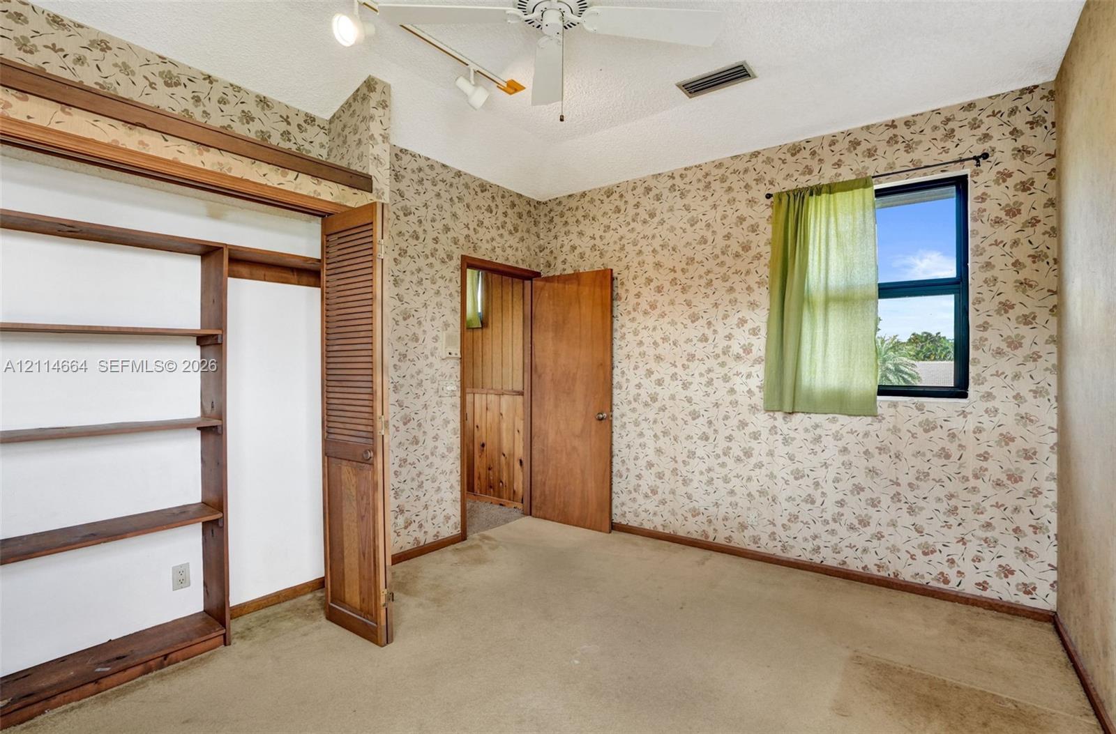 Room featuring vaulted ceilings with a ceiling fan, built-in wooden shelving, solid wood doors, and a single-pane window