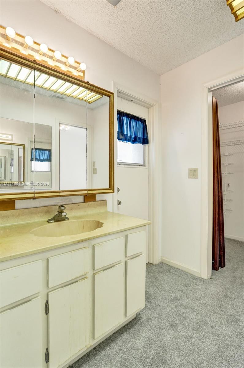 Bathroom featuring white cabinetry, an integrated sink with a stone-finish countertop, a large framed medicine cabinet, and overhead theater-style lighting