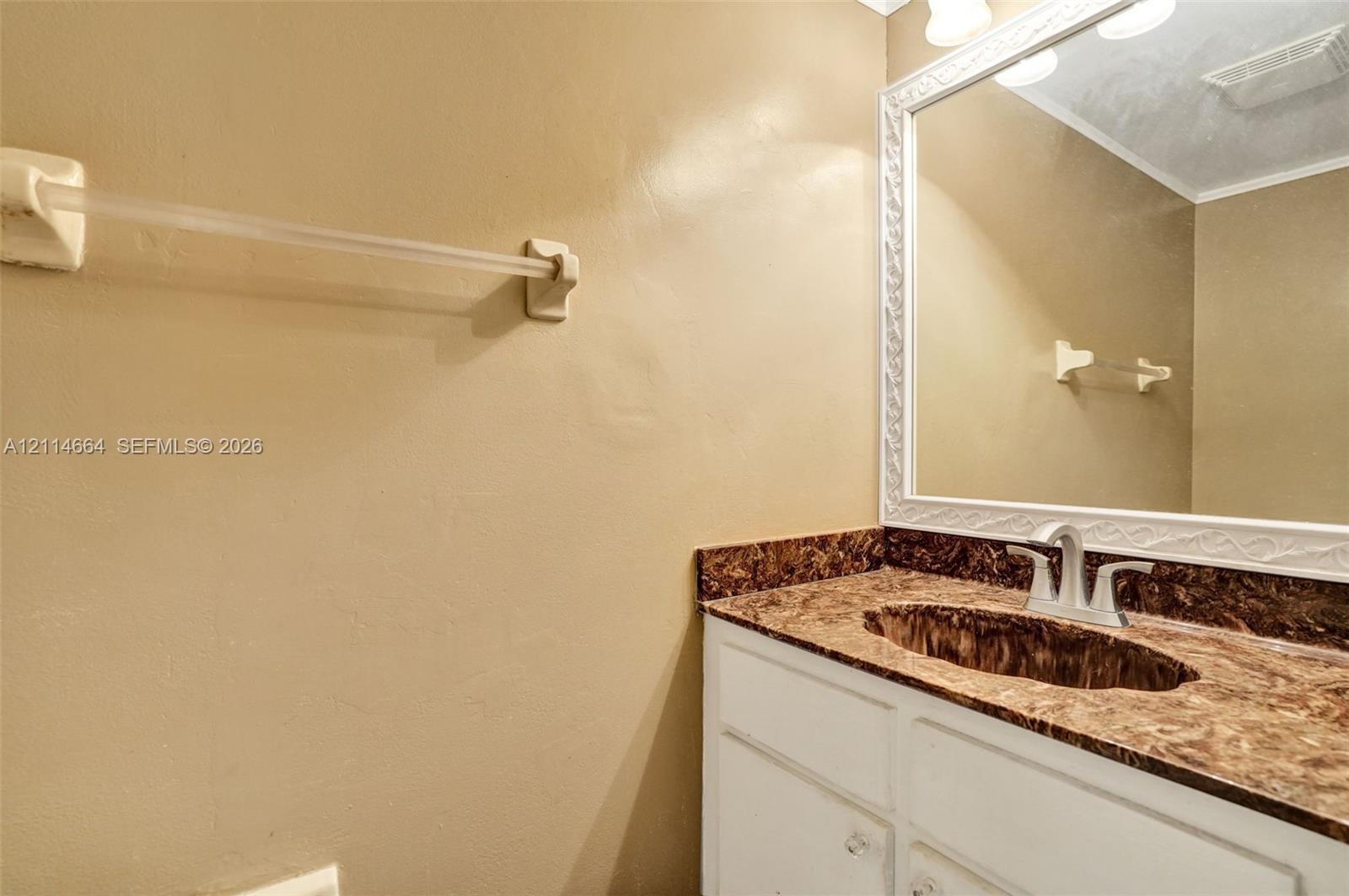 Vanity featuring a stone-patterned countertop, an integrated oval basin, white cabinetry, and a large wall-mounted mirror with a decorative white frame